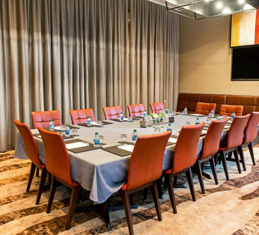 Conference room at the Avalon Hotel with a long table, red chairs, water bottles, notepads, pens, gray curtains, and modern decor set up for a meeting.